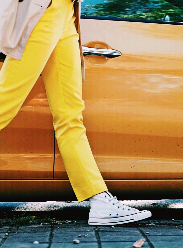 Quirky guy walking briskly beside a yellow car wearing equally bright yellow pants